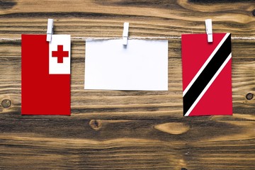 Hanging flags of Tonga and Trinidad And Tobago attached to rope with clothes pins with copy space on white note paper on wooden background.Diplomatic relations between countries.