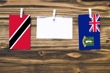 Hanging flags of Trinidad And Tobago and British Virgin Islands attached to rope with clothes pins with copy space on white note paper on wooden background.Diplomatic relations between countries.