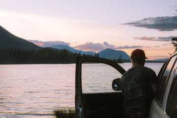 Man entering vehicle next to lake during sunset
