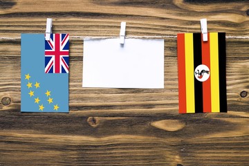 Hanging flags of Tuvalu and Uganda attached to rope with clothes pins with copy space on white note...