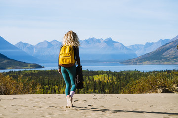 Young woman with backpack walking on desert with big mountains in background