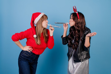 women blowing chirstmas whistles and wearing santa hat isolated over blue