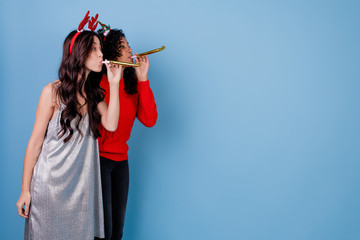 caucasian woman and black girl blowing christmas whistles isolated over blue
