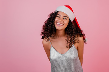 smiling black woman wearing santa hat and festive dress isolated over pink