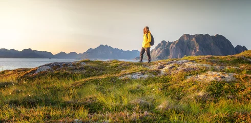 Fotobehang Vrouw met een rugzak kijkt naar de fjord. Oceaan en bergzonsonderganglandschap. Prachtig uitzicht. Reizen, avontuur Ontdek Noord-Noorwegen. Zomer in Scandinavië © olezzo