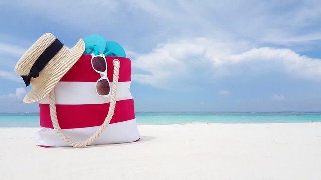 tourism and trave, tropical vacation concept, red white striped beach bag flip-flops glasses and children toy on white sand beach. Family vacation background