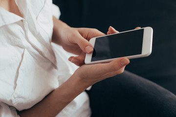 Woman hand holding white mobile phone and sitting on sofa at home.