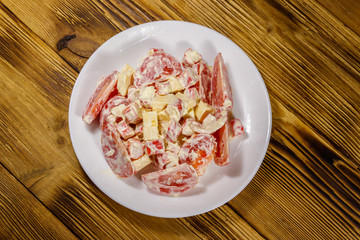 Tasty salad with crab sticks, cheese, tomato and mayonnaise on wooden table. Top view