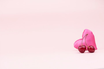 Two ripe cherries and a pink silk heart on a delicate background. Love concept