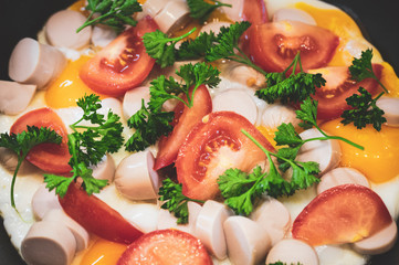 freshly cooked fried eggs with tomatoes greens and sausages in a frying pan, selective focus, tinted image