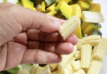 Hand Holding Chopped Baby Corns with Sponge Gourds and Pumpkins