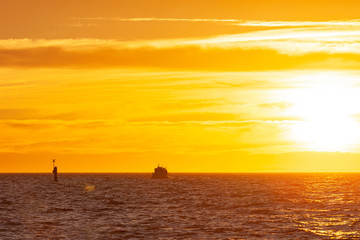 Passenger boat floating toward the coast in golden hour.