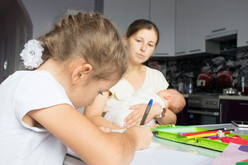 Obraz premium mother on hands with the baby checks lessons at the daughter, the concept of social problems of large families