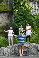 Happy Asian preteen boy and his sisters travel at waterfall in nature.