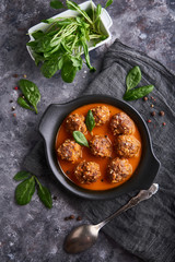homemade meatballs with tomato sauce and spinach served in a plate on a dark stone table