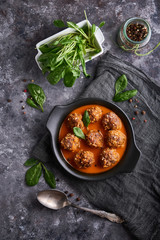 homemade meatballs with tomato sauce and spinach served in a plate on a dark stone table Vertical