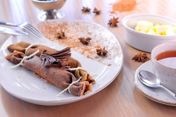 Chocolate russian pancakes, blini with curd filling on the plate. Served with a cup of tea and...
