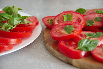 Closeup shot of the sliced tomato with basil on a plate and cutting board