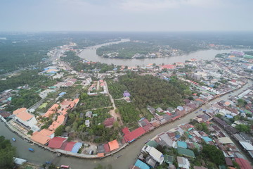 Fototapeta premium Aerial view above canal, river and city around with many boats and house with cloudy sky background, Amphawa floating market, Samut Songkhram, Thailand.