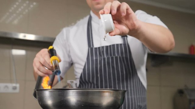 Chef cooking food with burning fire in slow motion. Unrecognizable male chef prepares food in frying pan with flame at kitchen. flambe dish with fire flames at restaurant. Shot in hd