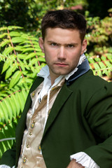 Portrait of handsome yet grumpy gentleman dressed in vintage costume sitting on bench in garden