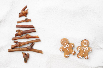 Flat lay stylized Christmas tree made of small twigs and gingerbread man cookies on snow background. Space for text