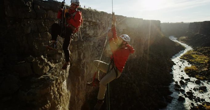 Steadicam past two rock climbers going up ropes in a deep canyon during sunset
