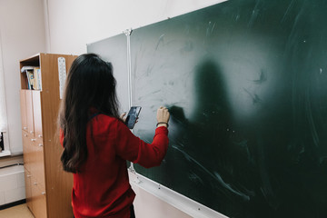 girl in a red jacket writes on a school blackboard