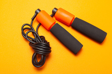 Jump rope. Fun exercises for body health. Orange rope with black cord. Yellow orange background