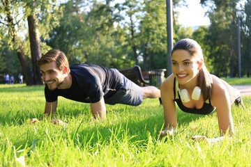 Young sports woman and man doing plank exercise together outdoors in urban park.