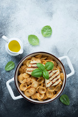 Orecchiette pasta with sun dried tomato pesto and grilled cheese in a serving pan. Top view over light-grey stone background with space
