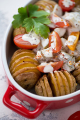 Close-up of baked hasselback potatoes in a red serving pan, selective focus, vertical shot