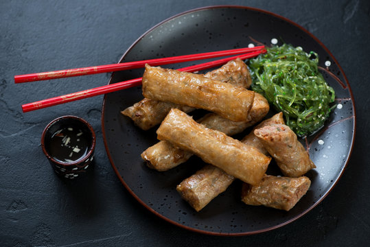 Traditional vietnamese deep fried spring rolls or nems with chuka salad served on a black plate, studio shot over black stone background