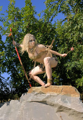 A young woman is  dressed as a prehistoric warrior.  She is covered with mud, filth and dirt and is...