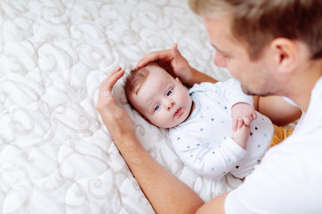 Top view of handsome young dad playing and talking to his adorable six months old son. Baby looking at away while lying in bed.