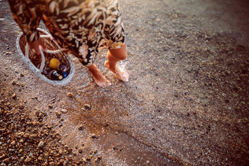 Cropped picture of female's legs walking in water. Woman holding picnic basket in hands.