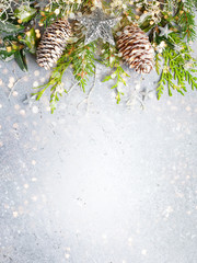 Christmas or winter background with a border of green and frosted evergreen branches and pine cones...