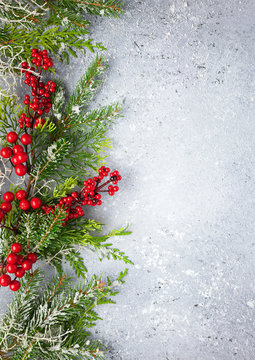 Christmas or winter background with a border of green and frosted evergreen branches and red berries on a grey vintage board. Flat lay