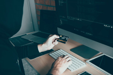 Hacker in the hood working with computer and holding credit card with payment hacking concept.