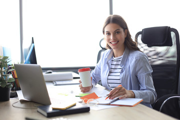 Beautiful smiling business woman is sitting in the office and looking at camera