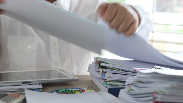 Education and business concept. Asian teacher hands is searching for student's homework assignments archive with colorful papers on table to make a check and inspect. Stack of paperwork and reports. 