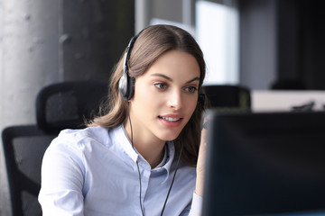 Beautiful smiling call center worker in headphones is working at modern office