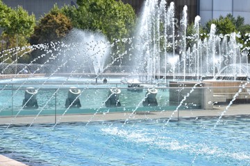 Spray fountain in the center of city with selective focus and blurred background. Running fountain with splashes and drops of water. Water jets in the fountain.