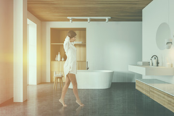 Woman walking in white bathroom, cabinet and sink