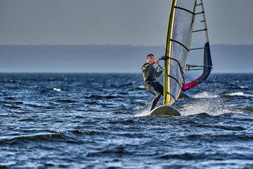 A male athlete is interested in windsurfing. He moves on a Sailboard on a large lake on an autumn...