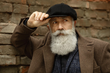 Handsome confident mature man with beard stands in coat on street with copy space for your text message or advertising, fashionable rich male dressed in expensive clothes posing outdoors.