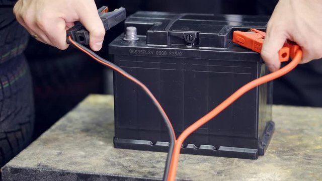 The male hand connects the terminals to the car's batteries. A man throws and removes the terminals on the battery.