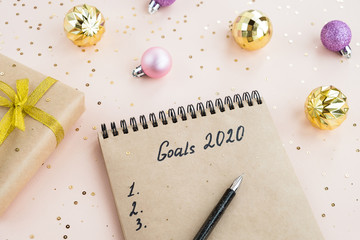 New year Goals Concept 2020. Notebook with notes of plans on a table with a festive decor and a gift box. Stylish composition in light pink and gold colors. Top view, flat lay