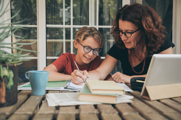 Young student doing homework at home with school books, newspaper and digital pad helped by his...