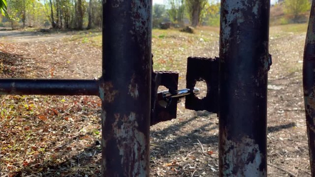 Locked padlock on rusty metal gate on a sunny autumn day.